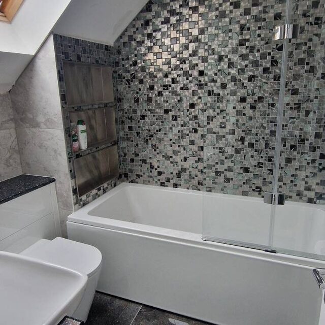 Loft conversion bathroom with a bath and shower screen, mosaic feature tiling and black sparkle floor tiles under a Velux window, installed by Downs Plumbing & Heating