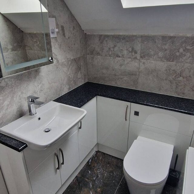 Loft bathroom with a wall-hung vanity unit and wall-hung toilet on a black worktop, fitted by Downs Plumbing & Heating