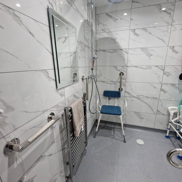 Mobility wet room tiled in marble-effect porcelain with grab rails, a shower seat, heated towel rail and level-access non-slip floor, fitted by Downs Plumbing & Heating