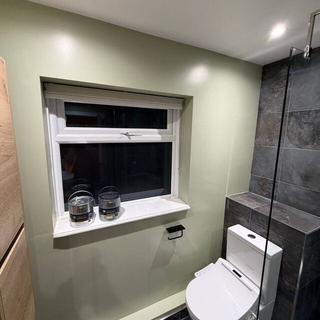 Bathroom in sage green with a rimless close-coupled toilet and a slate-tiled walk-in shower with glass screen, installed by Downs Plumbing & Heating