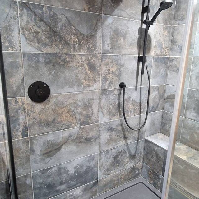 Walk-in shower enclosure tiled in stone-effect porcelain with a matt black rainfall head, hand shower and concealed thermostatic valve, fitted by Downs Plumbing & Heating in Kent